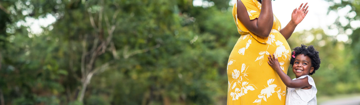 Pregnant women in yellow dress and her daughter who is hugging her belly.